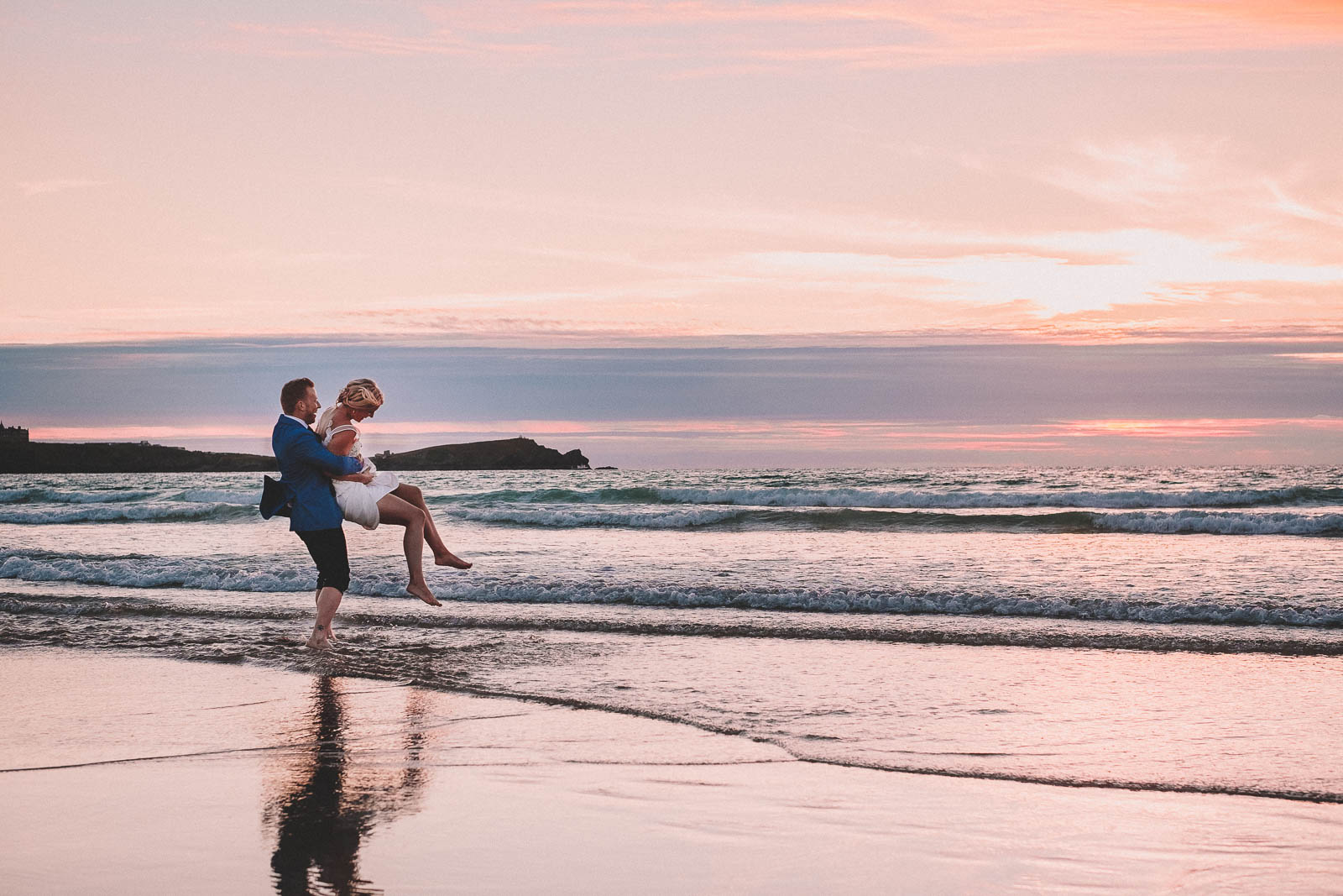 Lusty Glaze Wedding Photography. A bride and groom spinning each other round in the sea while the sunsets.
